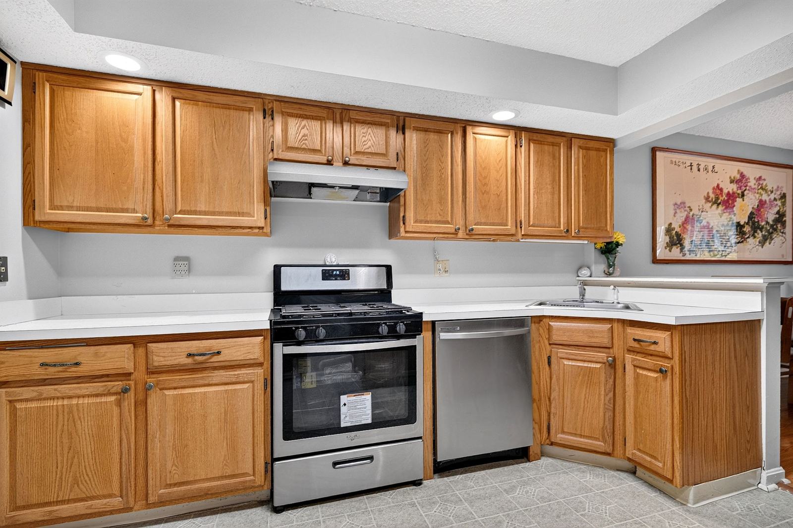 Kitchen with oak cabinets, stainless steel gas range and dishwasher, and recessed lighting