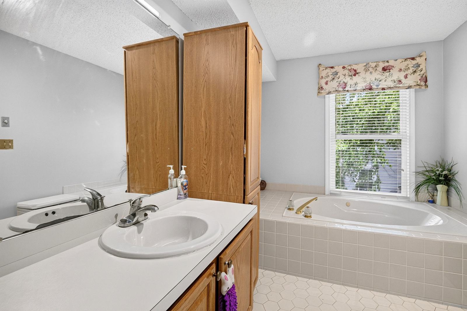 En-suite bath with a soaking tub under a window and a tall storage cabinet